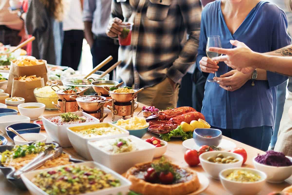 Buffet mit verschiedenen Speisen und Getränken, im Hintergrund Menschen in lockerer Kleidung