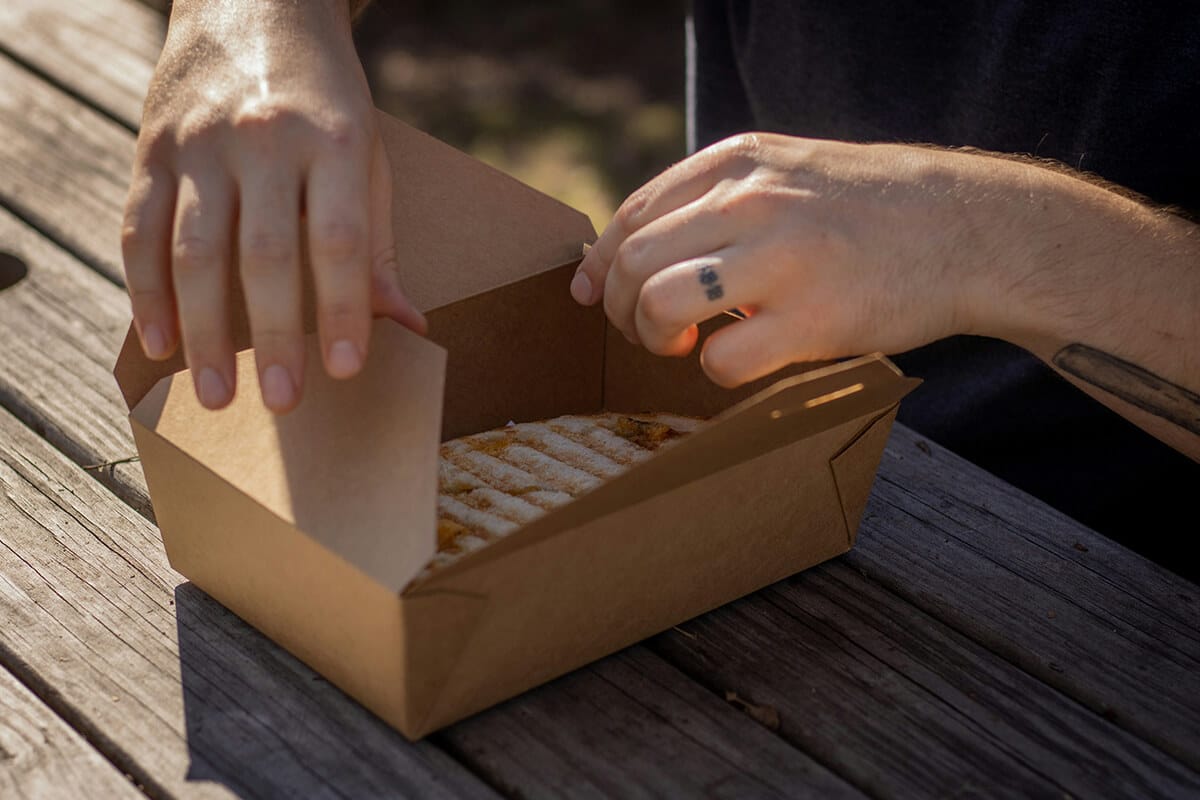 Hände öffnen eine braune Pappverpackung auf einem Holztisch